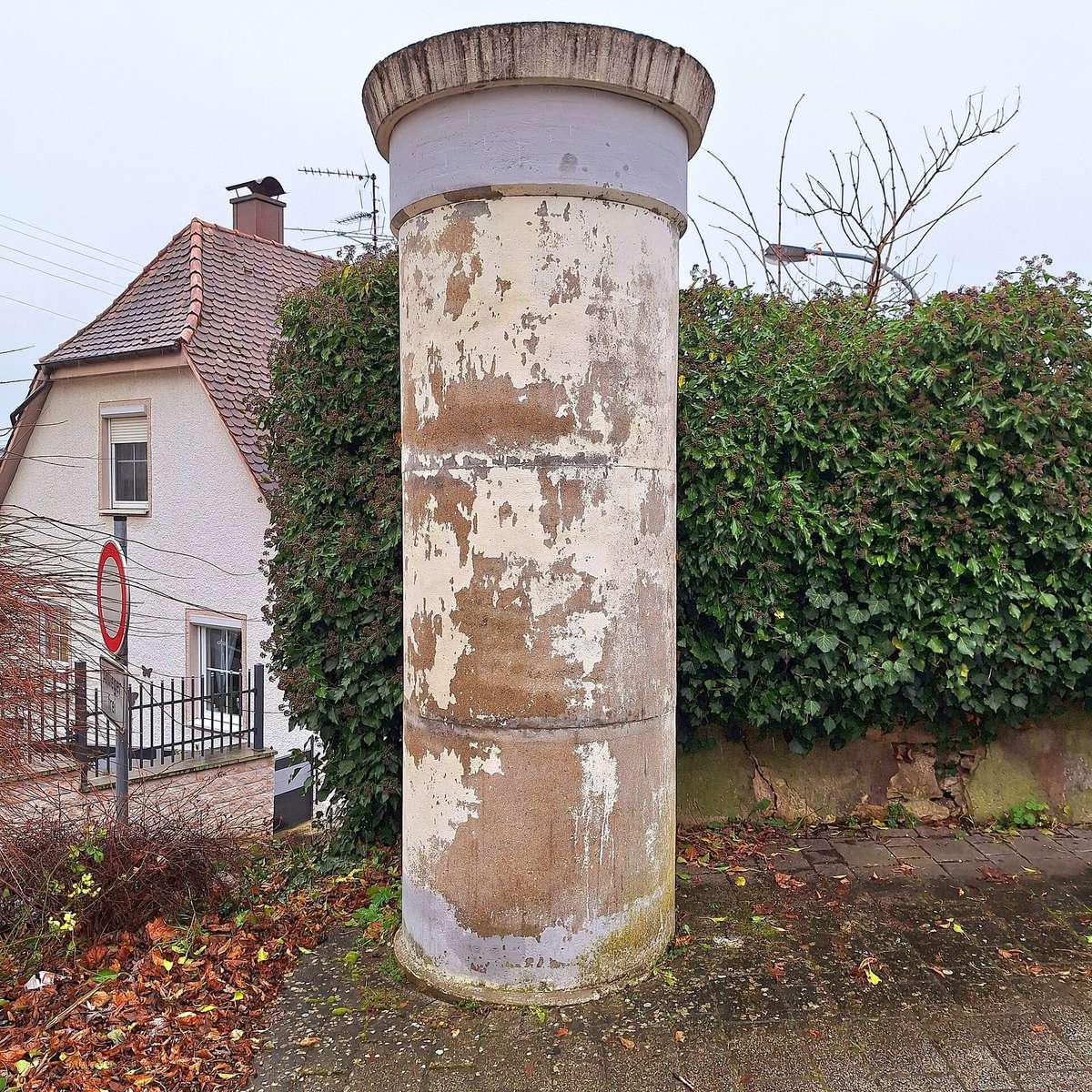 A weathered advertising column standing empty at the roadside in Obermarchtal, Germany.