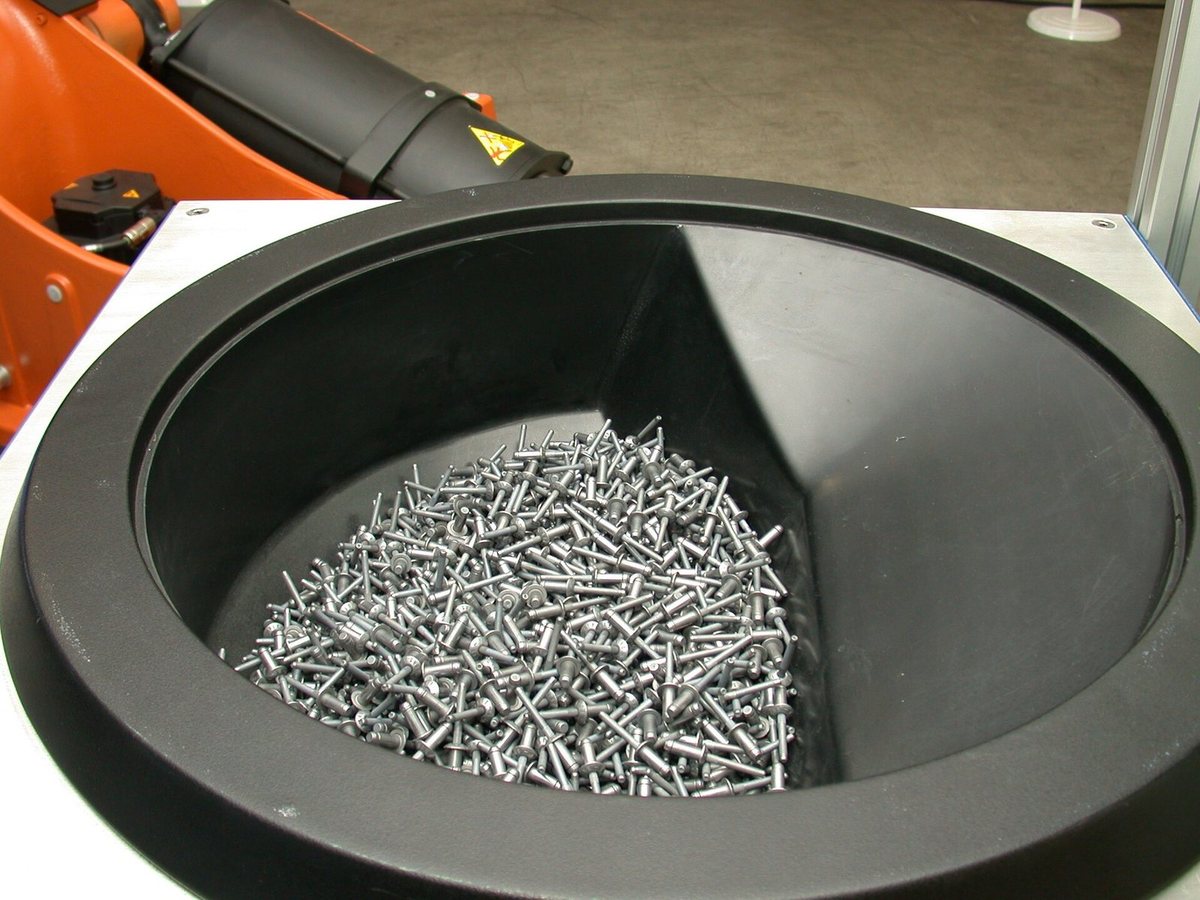 Blind rivets in the bowl of a vibratory feeder beside a robot riveting cell.