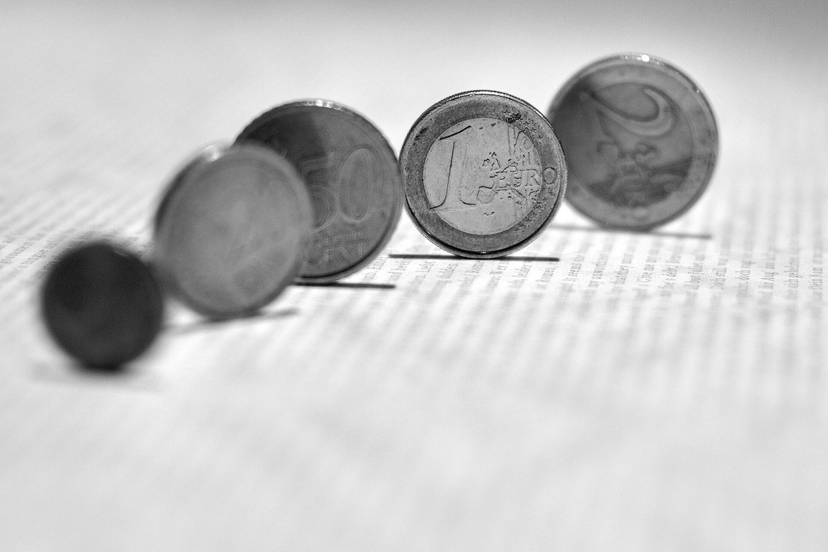 Euro coins standing on edge on a ruled surface, photographed in monochrome.